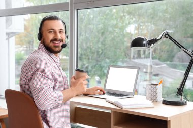 İşyerinde kulaklığı ve kahvesiyle oturan serbest çalışan biri.