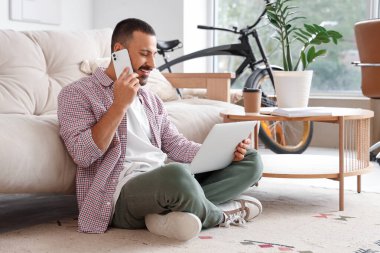 Evde dizüstü bilgisayarla otururken cep telefonuyla konuşan serbest çalışan.