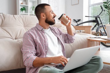 Evde dizüstü bilgisayarla yerde oturup kahve içen serbest çalışan bir işçi.