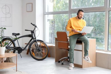 Evde dizüstü bilgisayarı olan genç bir adam sohbet ediyor.