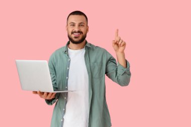 Pembe arka planda parmak ve dizüstü bilgisayarı olan genç bir adam.