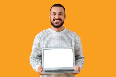 Sarı arka planda dizüstü bilgisayarı olan gülümseyen genç adam.