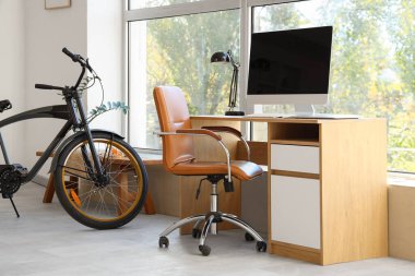 Pencerenin yanında modern bilgisayar ve bisikleti olan şık bir iş yeri