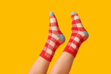 Sarı arka planda sıcak kareli çoraplı genç kadın bacakları.