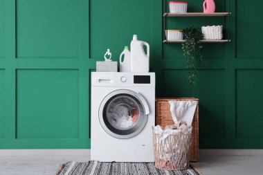 Çağdaş çamaşır makinesi ve çamaşır sepetleri yeşil duvarın yanında.