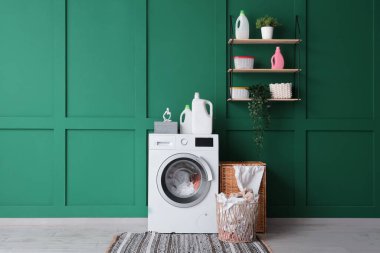 Çağdaş çamaşır makinesi ve çamaşır sepetleri yeşil duvarın yanında.