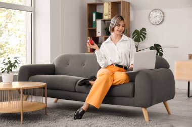 Elma tutan ve ofisteki koltukta dizüstü bilgisayarla çalışan başarılı bir iş kadını.