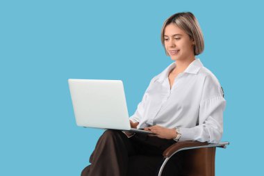 Mavi arka planda dizüstü bilgisayarı olan genç bir kadın.