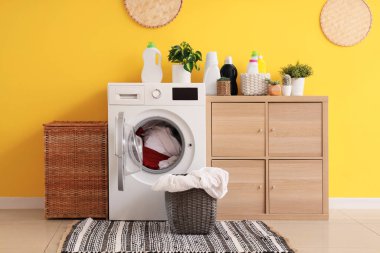 Modern çamaşır makinesi, çekmece sandığı ve sarı duvarın yanındaki çamaşır sepetleri.