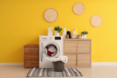 Modern çamaşır makinesi, çekmece sandığı ve sarı duvarın yanındaki çamaşır sepetleri.