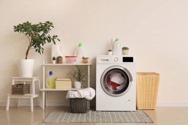Modern çamaşır makinesi, raf ünitesi ve çamaşır sepetleri beyaz duvarın yanında.