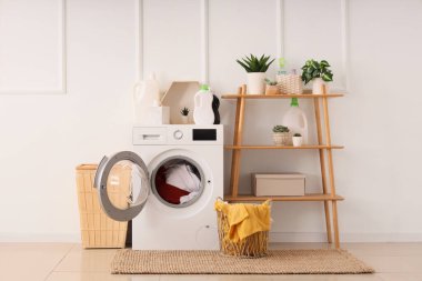 Modern çamaşır makinesi, raf ünitesi ve sepeti beyaz duvarın yanında.