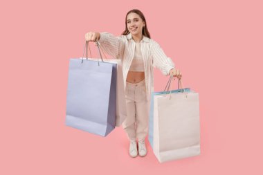Pembe arka planda alışveriş torbaları olan genç bir kadın.