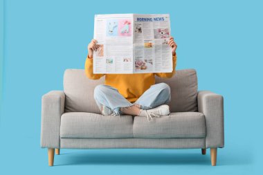 Kanepede oturan genç bir kadın, mavi arka planda gazete var.