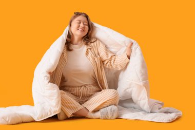 Sarı arka planda, battaniyeyle yerde oturan genç bir kadın.