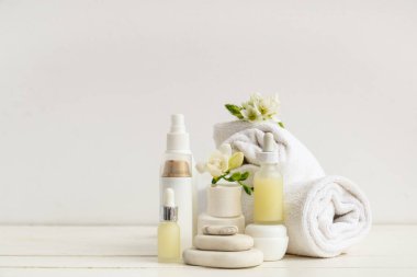 Kozmetik ürünleri, spa taşları, temiz havlular ve açık ahşap masadaki çiçekler.