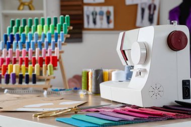 Atölyedeki terzi masasında desenli dikiş makinesi ve kumaş örnekleri var.