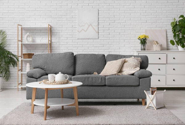 Comfortable sofa with pillows, coffee table and book holder in interior of living room