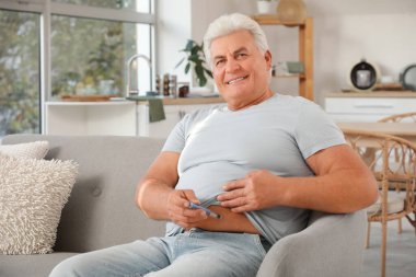 Şeker hastası, olgun bir adam evdeki kanepede tükenmez kalem kullanıyor.