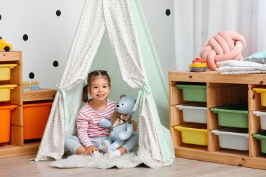 Çocuk odasında oyuncak ayıyla çadırda oturan tatlı küçük kız.