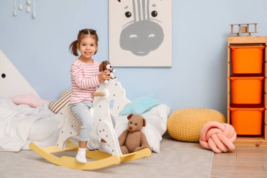 Pijamalı, oyuncak köpekli, çocuk odasında sallanan ata binen tatlı bir kız.