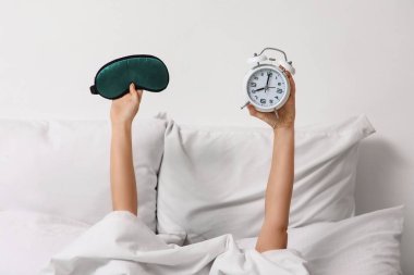 Evde alarm saati ve uyku maskesi takan kadın eller.