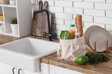 Mutfaktaki lavabonun yanında farklı taze ürünlerle dolu bir alışveriş çantası.