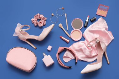 Yüksek topuklu ayakkabı, saç bandı, makyaj malzemesi ve mavi arka planda aksesuarları olan bir kompozisyon. Üst görünüm