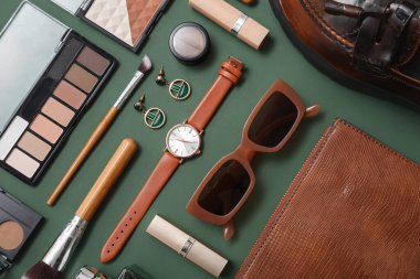 Kozmetik ürünleri, aksesuarlar, kol saati ve yeşil arka planda güneş gözlüğü olan bir kompozisyon. Yakın çekim.