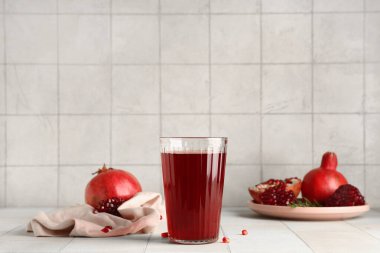 Bir bardak taze nar suyu ve beyaz fayanslı meyve tabağı.