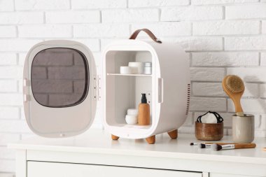 Odadaki beyaz tuğla duvarın yanındaki çekmecelerde ürünleri olan küçük bir kozmetik buzdolabı. Yakın çekim.