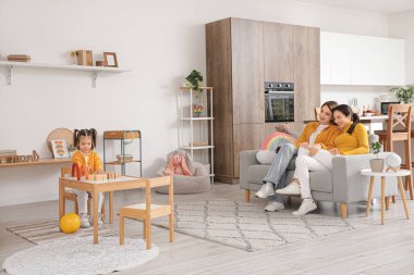 Küçük kızları evde oynarken genç lezbiyen çift kanepede oturuyor.