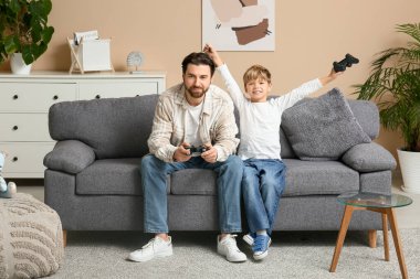 Baba ve küçük oğlu evde video oyunu oynuyorlar. Babalar Günü.