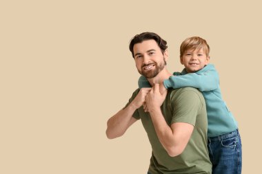 Gülümseyen baba ve küçük oğlu bej arka planda eğleniyorlar. Babalar Günü.