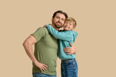 Gülümseyen baba ve küçük oğlu bej arka planda sarılıyorlar. Babalar Günü.