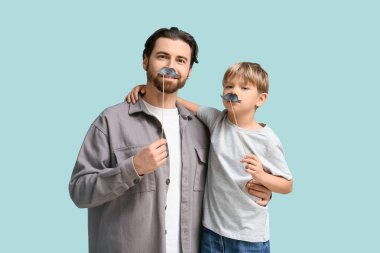 Mavi arka planda kağıt bıyıklı baba ve küçük oğlu. Babalar Günü.