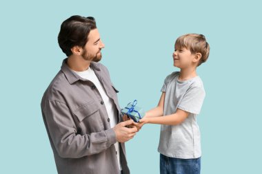 Küçük şirin çocuk mavi arka planda babasına hediye veriyor. Babalar Günü.