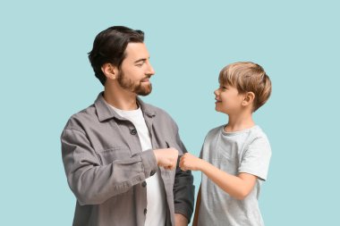 Baba ve küçük oğlu mavi arka planda yumruk tokuşturuyorlar. Babalar Günü.