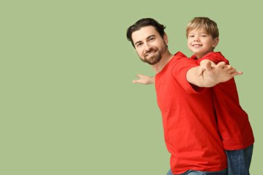 Küçük oğlu yeşil arka planda babasının sırtına biniyor. Babalar Günü.