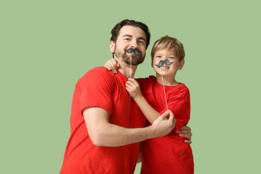 Yeşil arka planda kağıt bıyıklı baba ve küçük oğlu. Babalar Günü.