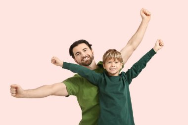 Gülümseyen baba ve pembe arka planda ellerini kaldırmış küçük oğlu. Babalar Günü.