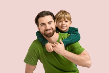 Gülümseyen çocuk pembe arka planda babasına sarılıyor. Babalar Günü.