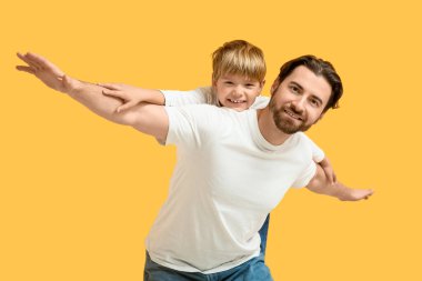 Küçük oğlu sarı arka planda babasının sırtına biniyor. Babalar Günü.