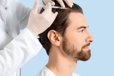 Genç adam mavi arka planda saç büyümesi için iğne oluyor, yakın plan.