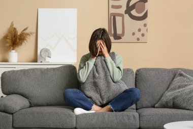 Depresyonda olan genç bir kadın ellerini kanepeye koyup yüzünü gizliyor.