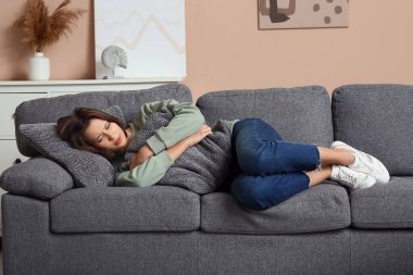 Depresyondaki genç kadın evdeki kanepede yastığa sarılıyor.