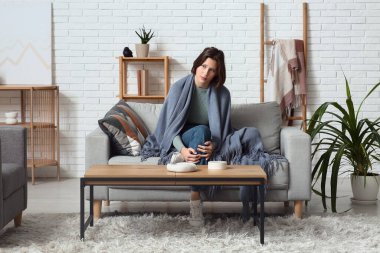 Oturma odasındaki kanepede ekoseli depresif genç kadın.