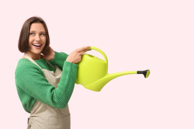 Pembe arka planda sulama tenekesi olan gülümseyen genç kadın.