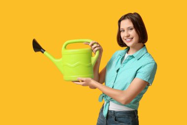 Sarı arka planda sulama kutusu olan güzel genç bir kadın.