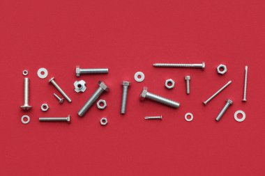 Kırmızı arka planda farklı tap cıvataları, vidalar ve krom fındıklar